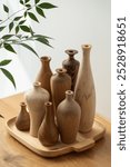 Wooden vases of varying shapes and grain patterns sit on a wooden tray, complemented by nearby green leaves, creating a natural and earthy scene.