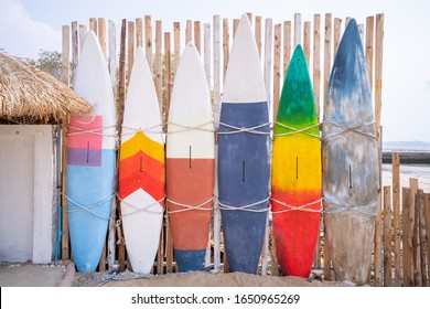 Wooden Vintage Surfboard And Bamboo Fence Stands In The Sand