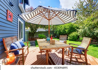 Wooden Walkout Deck In The Backyard Garden Of Blue Siding House. Furnished With Patio Table Set With Umbrella