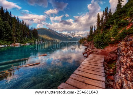 Wooden walkway along clear mountain lake and evergreen trees