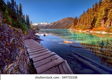 Wooden walkway along the glacial lake, with pine trees and mountains