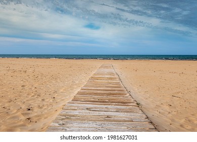 Wooden Walkway Extended On A Fine Sandy Beach With The Mediterranean Sea In The Background. In A Cloudy Sunset.