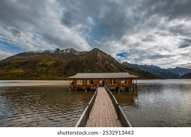 A wooden walkway leads to a lakeside cabin, nestled by tree-covered mountains under a moody sky. - Powered by Shutterstock