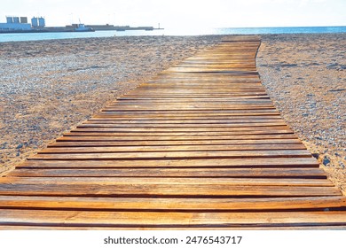 Wooden walkway on a sandy beach, leading towards the calm ocean water - Powered by Shutterstock