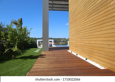 Wooden Walkway Or Pathway With Green Leaves Of Ornamental Shrubs And Raw Concrete Wall Backgroud,Outdoor Interior Design Of Park At House.