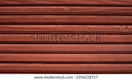 Wooden wall sheathed with clapboard with horizontal stripes.Wooden surface painted with red paint.