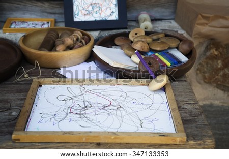 Wooden whirligig on wooden board with white leaf of paper. Pencil inserted into the wooden whirligig. Such a whirligig, spinning, drawing on paper. Traditional game Latvian children in ancient time.