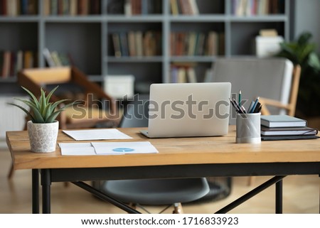 Wooden work desk with laptop and documents, books, modern interior of cozy cabinet, table for businessman or student at home, comfortable workspace, workplace with computer in apartment
