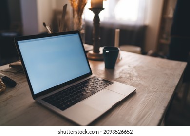 Wooden Working Desk With Cup, Opened Laptop Computer And Many Art Objects And Equipment In Dark Art Studio With Sunny Lighting. Workspace Of Artist, Sculptor Or Other Art Worker. No People