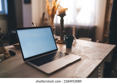 Wooden Working Table With Cup, Opened Laptop Computer And Many Art Items And Equipment In Dark Art Studio With Sunny Lighting. Workspace Of Artist, Sculptor Or Other Art Worker. No People