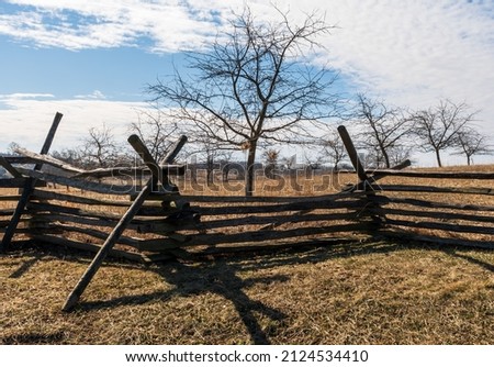 A wooden worm fence with bare peach trees behind it in the Peach Orchard on the Gettysburg National Military Park on a sunny winter day