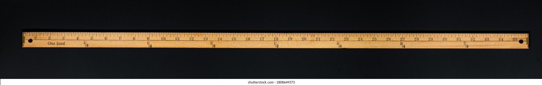 Wooden yardstick on black backgrounds whit inches and yard fractions scales.