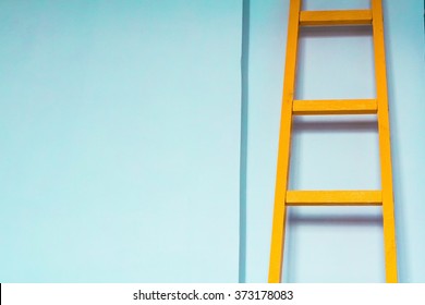 wooden yellow ladder on blue wall background.