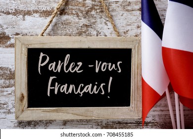 a wooden-framed chalkboard with the question parlez-vous francais? do you speak french? written in French, and some flags of France against a rustic wooden background