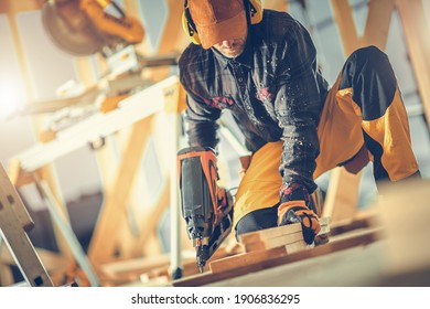 Woodwork Job. Caucasian Construction Worker in His 40s with Nail Gun in His Hand. Wooden House Frame Building. Industrial Theme.