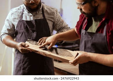 Woodworker holding timber block, showing workshop partner improvements to be made. Manufacturer pointing to apprentice defects in piece of wood to be fixed, close up shot - Powered by Shutterstock