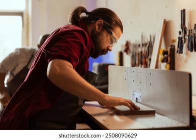 Woodworker operating spindle moulder to create bespoke joinery with coworker in background. Manufacturer and african american apprentice performing tasks on wood shaper, shaping and cutting planks