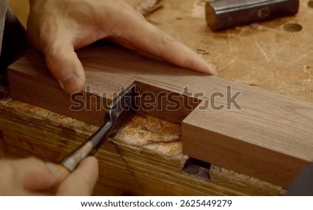 Woodworker using a chisel to carve a precise mortise joint on a hardwood piece in a traditional workshop.