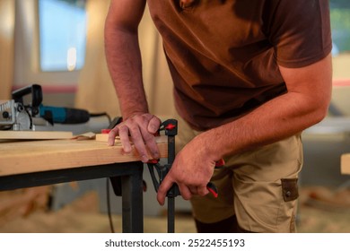 Woodworker using a clamp to secure a piece of wood on a workbench in a workshop.