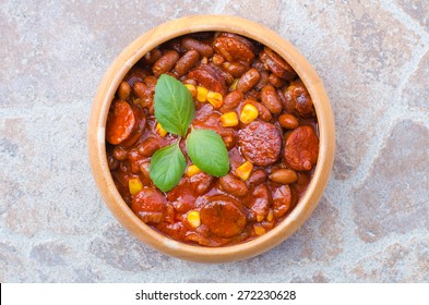 A Woody Bowl Of Homemade Chili Bean Goulash With Sausage And Corn On Stone Table, Soft Light