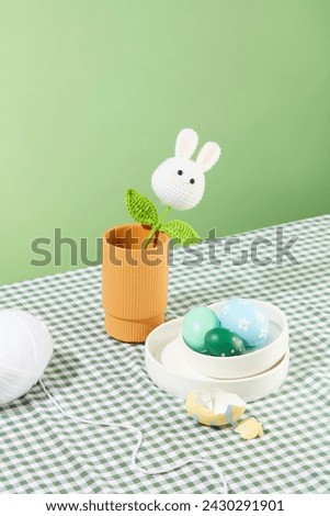 The wool is woven into the shape of rabbits and leaves inside a pot. A stack of white dishes and few Easter eggs arranged with a white hank. Easter Sunday is a religious Christian holiday