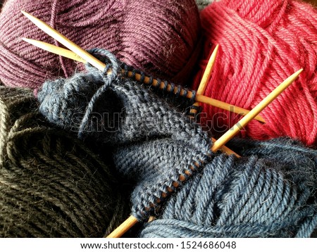 Wool yarn in different colors with wooden double point needles. The needles are being used for knitting socks, mittens or other projects joined in the round. 