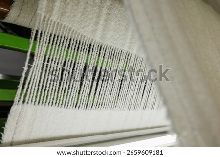Woolen fabric weaving in progress on an industrial loom, showcasing textile production and manufacturing process closeup.
