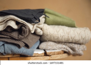 Woolen sweaters of pastel shade lie in set on wooden table, yellow background. Concept recycling clothes.