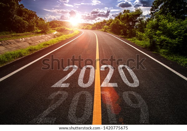 The word 2020 written on highway road in the middle of empty asphalt road at golden sunset and beautiful blue sky. Concept for new year 2020.