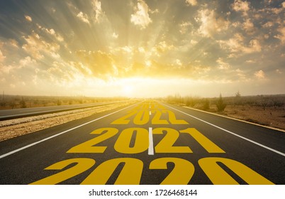 The word 2021 written on highway road in the middle of empty asphalt road at golden sunrise