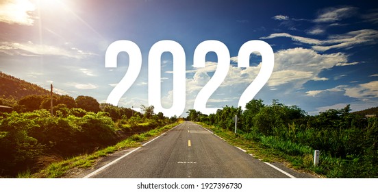 The word 2022 behind the tree of empty asphalt road at golden sunset and beautiful blue sky. Concept for vision year 2022. 
