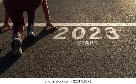 Word 2023 written on the asphalt road and athlete woman runner preparing to start on an athletics track engraved for new year at sunset.Concept of new year 2023,challenge or career path and change. - Powered by Shutterstock