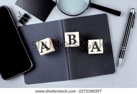 Word ABA on wooden block on a black notebook with smartpone, credit card and magnifier