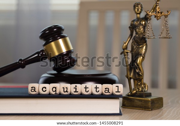 Word  ACQUITTAL\
composed of wooden dices. Wooden gavel and statue of Themis in the\
background. Closeup