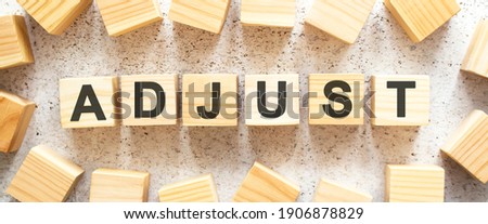 The word ADJUST consists of wooden cubes with letters, top view on a light background. Work space.