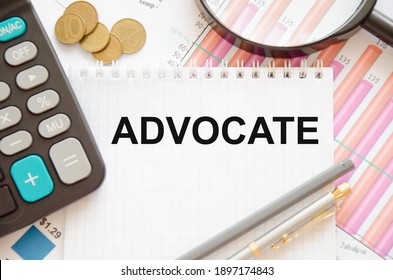 The Word Advocate Is Written On A White Notepad That Lies On A Financial Chart Near Coins And A Pen, A Calculator. High Quality Photo