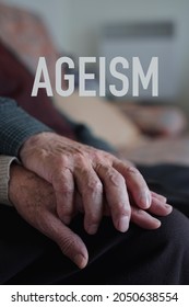 The Word Ageism And A Senior Caucasian Man And A Senior Caucasian Woman Holding Hands With Affection, Sitting In A Couch