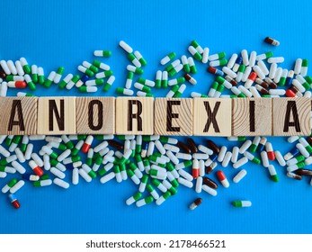 Word Anorexia Made From Wooden Cubes With Letters Next To Pills On Blue Background. Treatment Of Anorexia