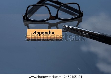 The word APPENDIX is written on the post-it note on the glass table. A pen, and eyeglasses at the back. Reflection.