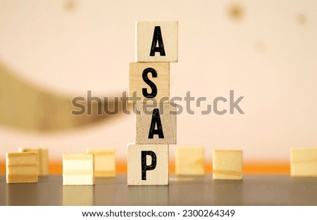 word ASAP with wood building blocks, light gray background. document with numbers on background, business concept. space for text in right. front view. ASAP - AS SOON AS POSSIBLE