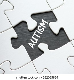 The word Autism revealed by a missing piece of a jigsaw puzzle laid out on a blackboard surface