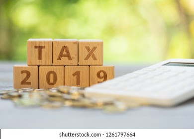 Word block "TAX", and "2019" on pile of coins with calculator as background. Income, expenses, tax, financial data.