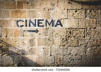 The word "cinema" and an arrow pointing the right side painted in black on a stone wall. - Powered by Shutterstock