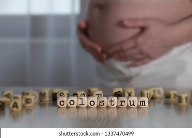 Word COLOSTRUM  composed of wooden letters. Pregnant woman in the background