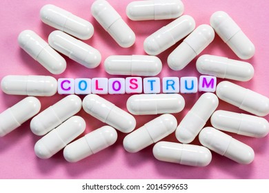 Word Colostrum.  Plastic cubes with lettering surrounded by pharmaceutical pills on pink background close-up. Selective focus