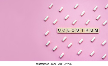 Word Colostrum. Wooden blocks with lettering surrounded by pharmaceutical pills on pastel background. Copy space