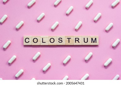 Word Colostrum. Wooden blocks with letters surrounded by pharmaceutical pills on pink background. Top view, layout