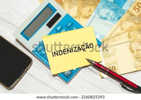 The word compensation in Brazilian Portuguese written on a piece of paper. Brazilian Real banknotes and a calculator in the composition.
