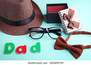 Word Dad With Bow Tie, Glasses, Hat And Gift Box On Mint Background