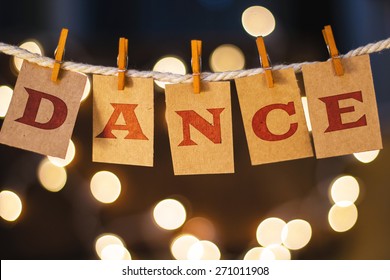The word DANCE printed on clothespin clipped cards in front of defocused glowing lights.